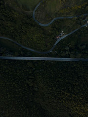 Aerial view of highway road in middle of forest trees on mountains, meadows, italian village Frasso Sabino, Lazio region, Italy, Europe. Green rural landscape countryside. Cars and trucks go on road.