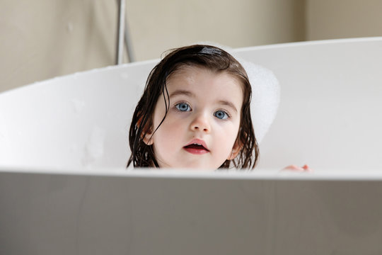 Portrait of cute toddler girl in bathtub looking at camera