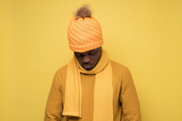 African young man in warm hat and scarf looking down being upset.