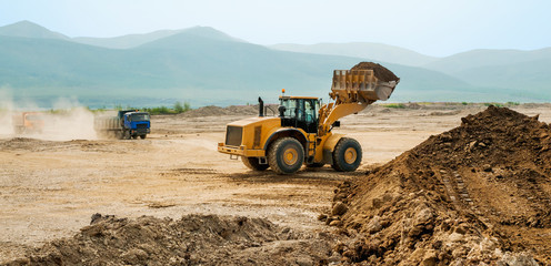 Loading earth soil into the side of a cargo dump truck with a front loader bucket