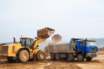 Fototapeta na wymiar Loading earth soil into the side of a cargo dump truck with a front loader bucket