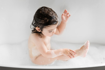 Cute toddler girl washing her leg in bathtub