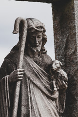 Dark contrast image of Jesus figure holding baby lamb and Shepard’s crook/staff