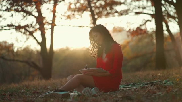 beautiful young woman writing in diary in autumn park