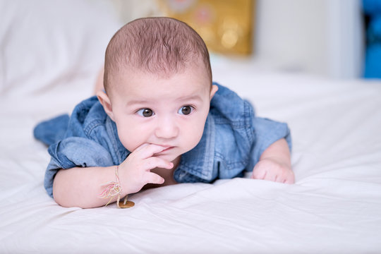 A 5 months old caucasian baby sucking his fingers in his mouth.