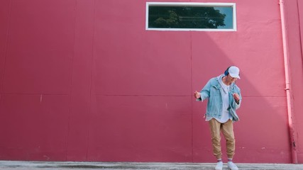 Dancing man with headphones listening to music performing various freestyle dance outdoors in street wall having fun. Modern lifestyle, happiness concept. breakdancing, hiphop dancing, street dancing.
