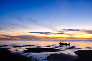 Beautiful landscape view of nature in the morning sunrise with silhouette fishing boat on the beach and orange and blue sky background in Thailand 