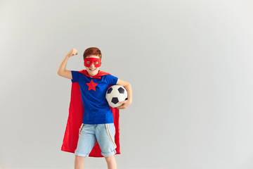 Smiling boy in superhero costume showing power and holding soccer ball in hand, copy space © Studio Romantic
