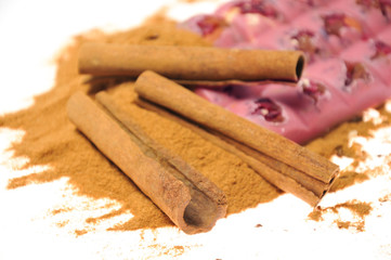 Bar of pink chocolate with raisins and fruits on a background of cinnamon sticks close up
