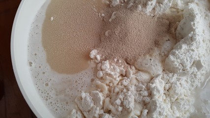 Flour,tremors, salt, sugar, water in a white bowl on a wooden table. Cooking process. Pancakes recipe. 