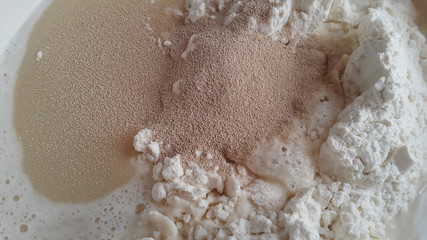 Flour,tremors, salt, sugar, water in a white bowl on a wooden table. Cooking process. Pancakes recipe.	
