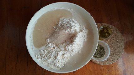 Flour,tremors, salt, sugar, water in a white bowl on a wooden table. Cooking process. Pancakes recipe. 