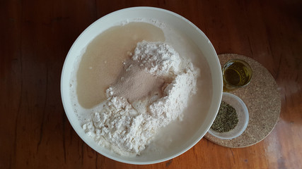 Flour,tremors, salt, sugar, water in a white bowl on a wooden table. Cooking process. Pancakes recipe. 