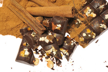 Bar of dark chocolate with raisins and dried apricots on a background of cinnamon sticks close-up