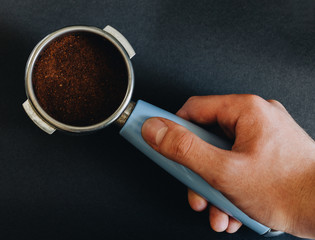 Espresso filter holder for coffee machine on black background in hand close-up