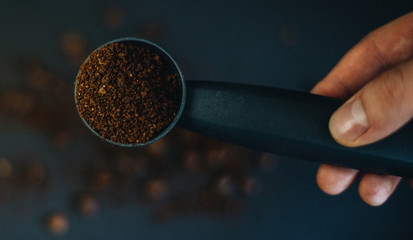 Grinded coffee powder in measuring scoop with beans isolated in hand on black background