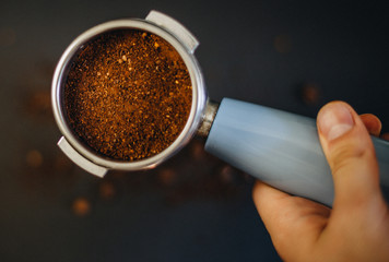 Coffee filter holder with and roasted beans scattered around on a black background in hand