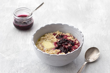 Delicious oatmeal porridge with butter and jam in a gray bowl on a light gray background. healthy homemade breakfast. selective focus, space	
