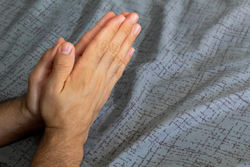 Fototapeta premium hands of a man together praying hopefully at the base of a gray bed