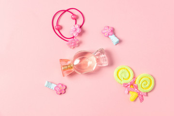 Children's flat lay. Perfume in the form of candy, children's jewelry and hair accessories on a pink background. Accessories for little girls.