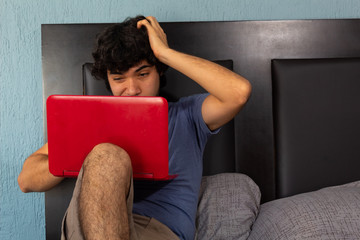 Young Hispanic man working stressed and furious from home on a bed due to quarantine