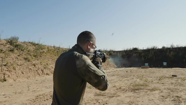 Portrait of a young man in camouflage clothes aiming moving shooting outdoors alone. Slow motion video.