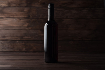Fototapeta na wymiar A closed bottle of red wine stands on a wooden table, dark wooden boards in the background. Copy space. Winemaking presentation concept.