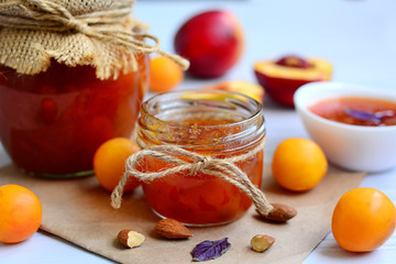 Close up of a jar with apricot jam and almonds on craft paper on a white background.