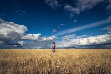 a girl stands in a field with crops under a blue cloudy sky
