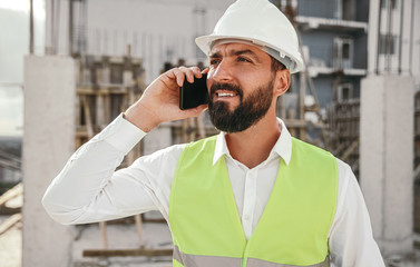 Serious architect talking on smartphone on construction site