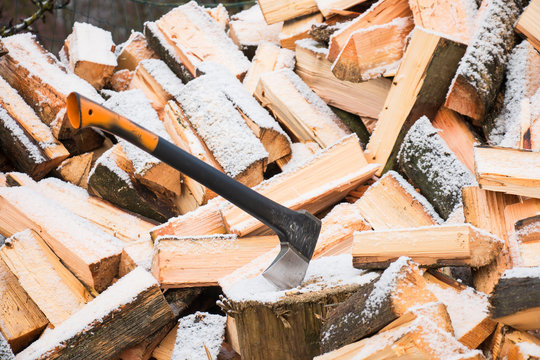 New axe attached to the trunk of the tree on the background of firewood covered with snow