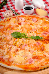Hawaiian Italian pizza with parmesan cheese, pineapple, corn, ham toppings, fresh basil and tomatoes sauce on a wooden board, rustic village background, top view. European cuisine