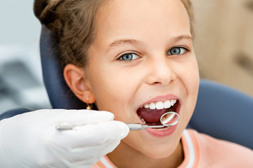 Little smiling girl, teeth check-up. Tooth exam using dental mirror close-up. Child's teeth treatment
