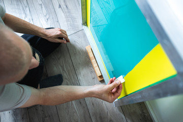 Overhead view of craftsman wiping silk screen emulsion while making stencil on floor 