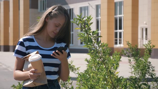The girl holds a smartphone in her hand. Using smartphone apps to deliver fast food and coffee. Studen walks at lunchtime. A valanter girl helps to deliver food. Social work.