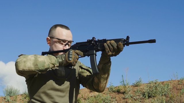Portrait of a young man in camouflage clothes aiming and shooting outdoors alone. Slow motion low angle footage.