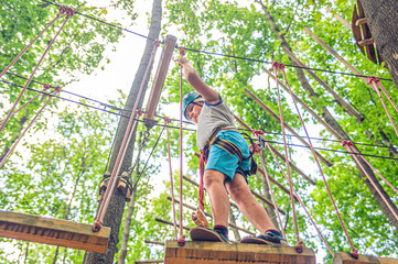 Teen boy in gear and helmet holds on to the ropes in forest adventure park