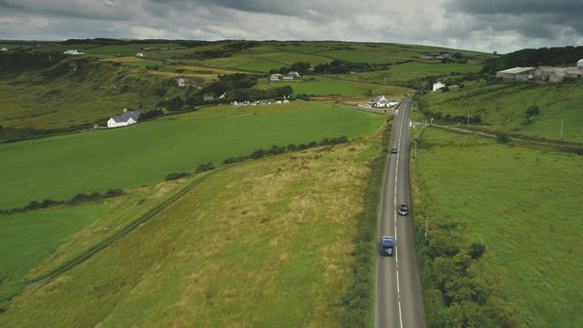 Aerial Ireland's road view: cars riding on countryside green way. Crossroads with vehicles moving. Roadside with greenery and trees. Picturesque rural scene landscape. 4K, UHD footage shot