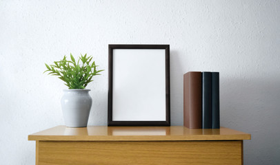 Black frame with plant and books over wooden furniture