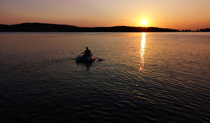 Naklejka na ściany i meble Man in an inflatable boat floats on the sea at sunset