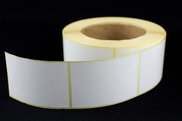 Babina of self-adhesive stickers on a black background. Self-adhesive white label roller for...