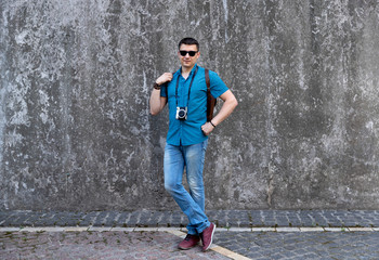 Man in casual clothes walking throught the city with camera and backpack