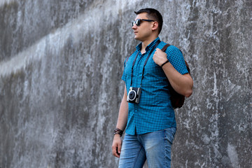 Man in casual clothes walking throught the city with camera and backpack