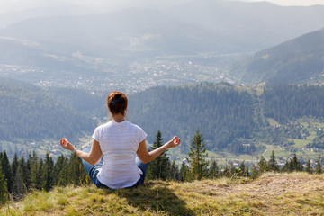 Woman in the lotus position meditates on the top of the mountain.