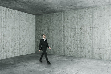 Businessman walking in blank concrete interior with copyspace on wall.