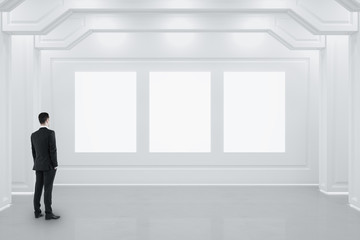 Businessman standing in classical interior with three blank banners on wall.