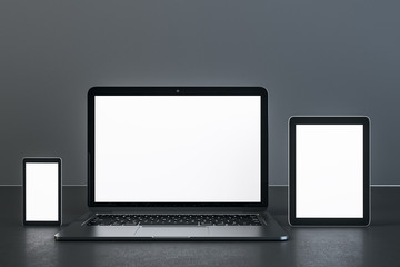 Laptop, digital tablet and smartphone with blank white screen on table.