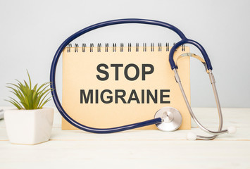 Text Stop Migraine in a notebook on medical forms with a phonendoscope and green pills. Medical conzept