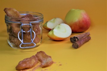 Homemade dried organic apple sliced with cinnamon in a jar l and pieces of this fruits on a table.