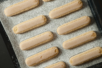 Ladies fingers cookies on a baking sheet with powdered sugar, savoiardi.